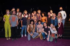 a group of people standing on top of a purple carpet in front of a stage