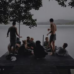 a group of people sitting on top of a pier next to the water and trees