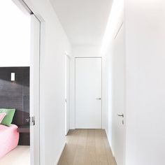 an empty hallway with white walls and wood flooring, leading to a bed in the corner