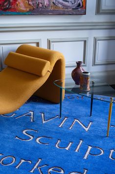 a living room area with a blue rug and yellow chair in front of a painting on the wall