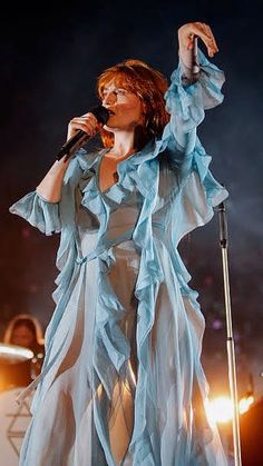 a woman in a blue dress holding a microphone and singing into the air on stage