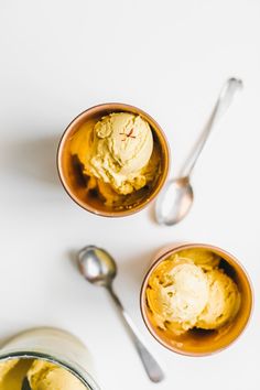 two bowls filled with ice cream and spoons next to each other on a white surface