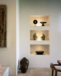 three shelves with vases on them in a white walled room next to a table