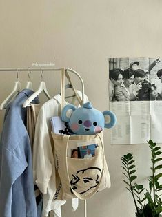 a blue teddy bear in a bag hanging on a clothes rack next to a potted plant