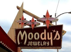 a sign that says moodus jewelry hanging from the side of a building