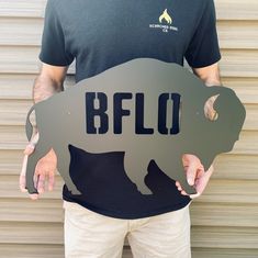 a man holding up a metal sign with a rhino on it's side that says buffalo