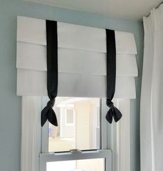 a window with two black bows hanging from it's valance and white curtains