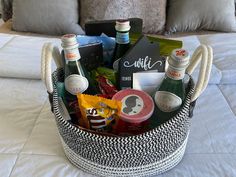 a basket filled with drinks and snacks on top of a white bed covered in pillows