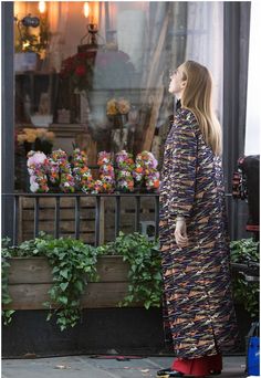 a woman standing on the sidewalk in front of a flower shop looking up at something