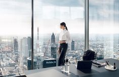 a woman standing in front of a window looking out at a cityscape with skyscrapers