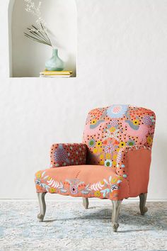 an orange chair sitting on top of a rug next to a vase with flowers in it