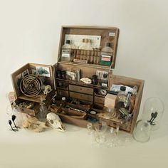 an open wooden box filled with assorted items on top of a white table next to two glass vases