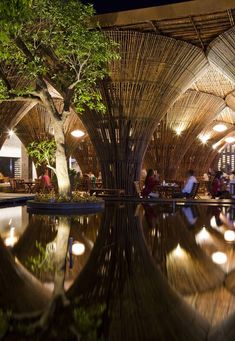 people are sitting at tables in an outdoor restaurant with bamboo roofing and lights on the ceiling