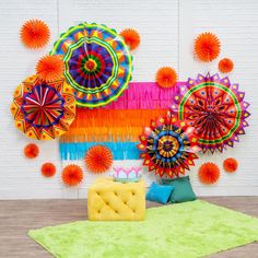 an assortment of colorful paper fan decorations on a white brick wall behind a yellow chair