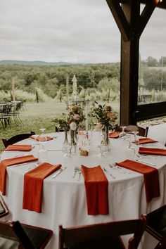 the table is set with orange napkins and place settings for an outdoor wedding reception