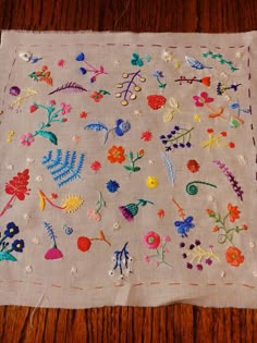 an embroidered cloth with flowers and leaves on it sitting on a wooden table next to a pair of scissors