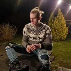 a young man sitting on top of a wooden bench in front of a forest at night