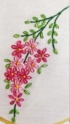 a close up of a embroidery on a white cloth with pink flowers and green leaves