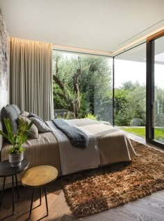 a bedroom with a large bed sitting next to a glass wall and wooden flooring