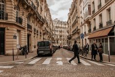 a man walking across a cross walk in front of tall buildings