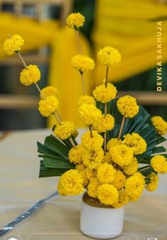 a white vase filled with yellow flowers on top of a table