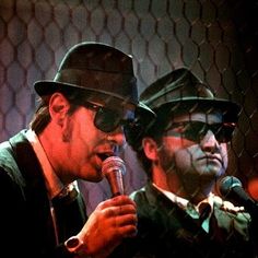 two men in hats and sunglasses are singing into a microphone