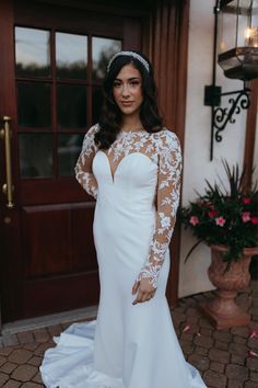 a woman standing in front of a door wearing a white wedding dress with sheer sleeves