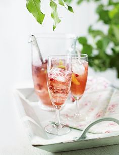 two glasses filled with drinks sitting on top of a white tray next to each other