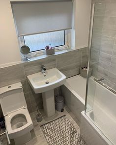 a white toilet sitting next to a bath tub in a bathroom under a window above a sink