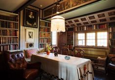 a dining room table in front of bookshelves with paintings on the walls and leather chairs around it