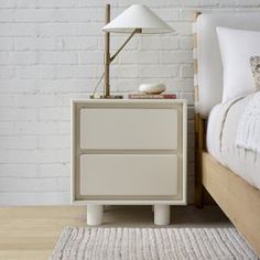 a white bed sitting next to a wooden nightstand on top of a hard wood floor