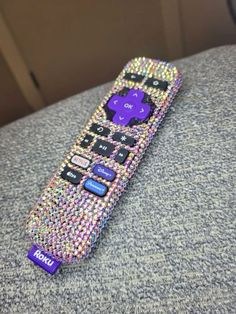 a purple and black remote control sitting on top of a gray couch next to a wall