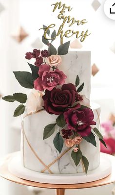 a white cake with red flowers on top and gold lettering that says mr and mrs cherry