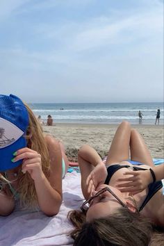 two women laying on the beach with one holding a frisbee in her hand