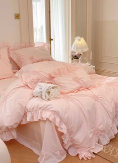 a bed with pink comforter and pillows on it in a room next to a window