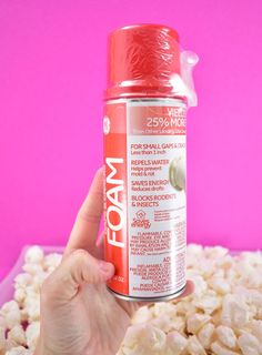 a hand holding a can of foam next to a pile of popcorn