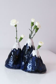 three small vases with flowers in them on a white tableclothed surface, one is blue and the other is white