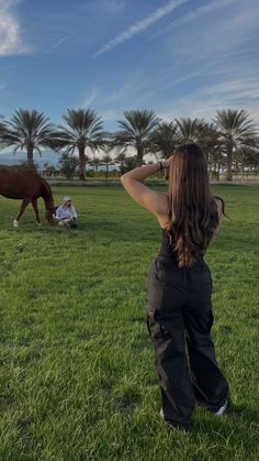 a woman standing on top of a lush green field next to a brown and white horse