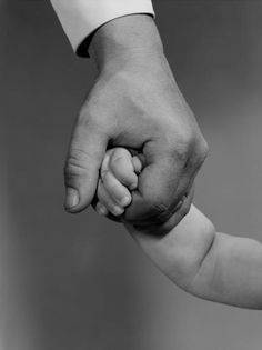 a black and white photo of a person holding the hand of a baby's hand