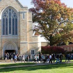 a group of people walking in front of a church on a sunny day with trees