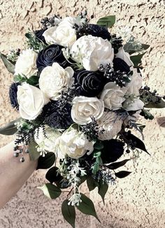 a bridal bouquet with black and white flowers is held by someone's hand