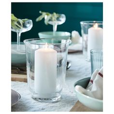 a white candle sitting in a glass bowl on top of a table next to plates and glasses