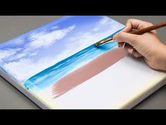 a person is holding a pencil and drawing on a piece of paper with the ocean in the background