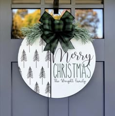 a merry christmas door hanger hanging on the side of a gray door with pine trees