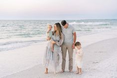 a family standing on the beach with their toddler girl and dad looking at her