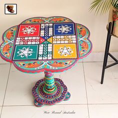 a colorful table sitting on top of a white tile floor next to a chair and potted plant