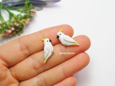 two small white birds sitting on top of each other's fingernails in front of a flower