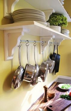 pots and pans are hanging from the wall above a cutting board on a kitchen counter