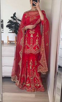 a woman taking a selfie while wearing a red lehenga with gold embroidery