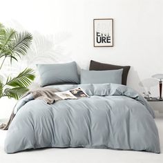 a bed with blue sheets and pillows in a room next to a potted plant